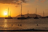 West Indies, British Virgin Islands, Tortola Island, sunset on the beach of Cane Garden Bay in the foreground bathers in the background sailboats at anchor