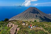 Italy, Sicily, Aeolian Islands, listed as World Heritage by UNESCO, Salina Island, hikers at the top of the old volcano Monte Fossa delle Felci observing the twin volcano Monte dei Porri during the picnic break, the islands of Filicudi and Alicudi in the background (aerial view)