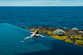 Spain, Canary Islands, La Palma, young seductive casual woman swimming in luxury infinity pool by the sea