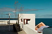 Spain, Canary Islands, La Palma, young woman resting on the edge of a terrace by the sea