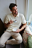 Man in cream-colored polo shirt enjoys espresso