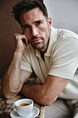 Man in cream-colored polo shirt enjoys espresso at wooden table