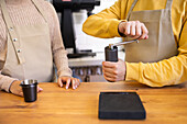 Close-up of a barista in an apron using a hand-operated coffee grinder at a wooden counter.