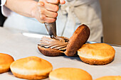 Crop anonymous cook with pastry bag adding chocolate cream on vegan sponge cakes while preparing desserts in bakehouse