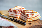 Thick, raw slices of lard placed on a wooden board, with a knife to the side, set for culinary uses.