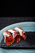 Serrano ham, a revered Spanish delicacy, elegantly presented on a black slate board against a dark background, highlighting its rich textures and colors