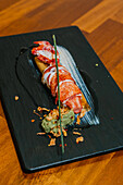 A succulent lobster tail is elegantly plated with artistic garnishes on a slate board, showcasing gastronomic finesse