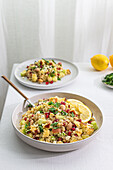 A vibrant bowl of quinoa salad with curry, garnished with fresh herbs, pomegranate seeds, nuts, and lemon slices, presented on a modern, elegant table setting.