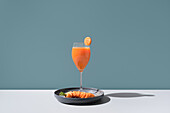 An exquisite arrangement featuring a refreshing cocktail garnished with a slice of citrus and smoked salmon delicately placed on a sleek black plate, casting soft shadows on a minimalist surface.