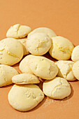 A collection of almond cookies freshly baked, with a cracked surface, scattered across a warm-colored background.