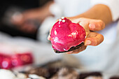 Unbekannter Koch zeigt leckeren veganen Kuchen in Herzform mit rosa Zuckerguss in einer Bäckerei.