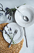 An inviting summer table setting featuring elegant white dishes, silverware, and fresh lavender flowers on a woven placemat