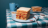 Stack of PB and Jelly sandwiches just served , with a cup of an american coffee and some bread slices in a blue background