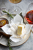 An elegant presentation of brie cheese with honeycomb, rosemary, and wine glasses on a textured surface for sophisticated dining.