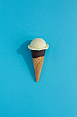 A vibrant cream ice cream scoop sits atop a classic waffle cone against a blue background, casting a playful shadow