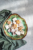 A selection of colorful Turkish delights presented on a rustic plate with a clear glass filled with black tea, complemented by a decorative vase of white roses in the background