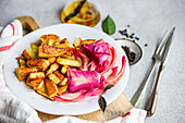 Ein pikantes Gericht aus fermentiertem Kohl mit Roter Bete, gewürzt mit Knoblauch und rotem Pfeffer, serviert mit gebackenen Kartoffeln auf einem weißen Teller.