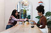 Side view of diverse female friends sitting at table and eating tasty poke while spending weekend in restaurant