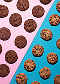 Top view of various chocolate chip and double chocolate cookies symmetrically placed on a contrasting pink and blue surface. The image highlights the texture and deliciousness of these freshly baked treats