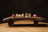 An elegant assortment of sushi, beautifully arranged on a rustic wooden sushi board, set against a dark background The variety includes nigiri and uniquely garnished rolls, highlighted by natural lighting