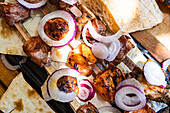 Close-up of succulent Georgian mtsvadi, skewered and grilled meats, accompanied by sliced red onions and fresh bread, showcasing the rich culinary traditions of Georgia