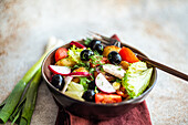 A beautifully arranged Mediterranean salad in a bowl, showcasing roasted potatoes, black olives, cherry tomatoes, crisp radishes, and lettuce, accented with fresh dill