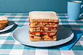 Peanut Butter and Jelly sandwich served on a blue plate , a cup of an american coffee and some bread slices in a blue background