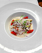 A vibrant shrimp ceviche garnished with cherry tomato, lime, and fresh herbs, served in a white bowl.