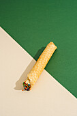 A diagonally positioned waffle roll filled with colorful sprinkles rests on a cream and green two-tone background, creating a playful and tempting visual.