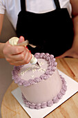 A close-up of hands artistically applying cream to a cake with a piping bag, showcasing cake decorating skills