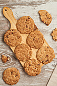 A tantalizing top view of fresh-baked chocolate chip cookies arranged neatly on a rustic wooden cutting board, with cookie crumbs scattered around