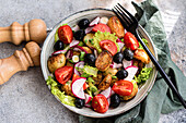 Close up of a rustic Mediterranean potato salad with spring potatoes, black olives, cherry tomatoes, spring onions, crisp lettuce, and radishes, served with a touch of elegance