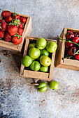 Holzkisten mit reifen Bio-Beeren - grüne Pflaumen, Kirschen und Erdbeeren - vor einer strukturierten Kulisse