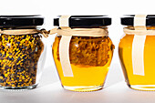 Glass jars with fresh honey and bee pollen placed in row on table