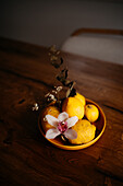 A tasteful arrangement of ripe lemons and a delicate orchid in a ceramic bowl on a wooden surface