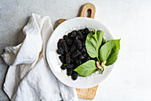 Top view of ripe mulberries in a white dish, complemented by vibrant green leaves and a subtle backdrop. Ideal for food and nutrition themes.