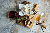 An overhead shot of Brie cheese, fresh rosemary, honey, and a glass of red wine arranged on a rustic wooden board.