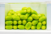 Bright green cucamelons neatly packed in a transparent glass container, viewed from the side against a white background