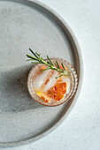 Top view of crafted vodka tonic cocktail adorned with grapefruit and rosemary, resting on a textured tray for an upscale serving experience