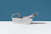 Fresh anchovies extend from an open can, set against a crisp blue background, illustrating a blend of natural and industrial themes