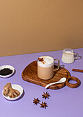 From a high angle perspective, A frothy chai latte garnished with star anise , on a wooden board with white spoon on a colorful background