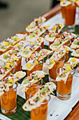 A sophisticated culinary setup featuring shot glasses of gazpacho soup garnished with exquisitely prepared gourmet toppings