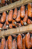 Cured sobrasada sausages from the Balearic Islands and various other types of cured meats hang in a traditional drying room, showcasing the rich culinary craftsmanship.