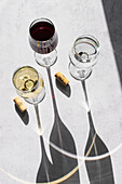 Three wine glasses filled with red, white, and no wine cast long shadows on a textured surface, showcasing a minimalistic and elegant design.