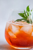 Close-up of a refreshing Coca-Cola cocktail with ice and fresh mint leaves in a clear glass, with droplets of water on the surface reflecting light.