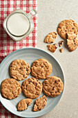 Delicious chocolate chip cookies on a blue plate with a glass of milk and red checkered napkin on a textured stone countertop