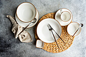 Top view of a stylish table setting featuring bright ceramic dinnerware and sleek cutlery on a woven placemat, ready for a refined dining experience.