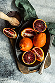 A vibrant arrangement of sliced blood oranges next to a manual juicer on a dark serving tray, with a fabric napkin adding texture