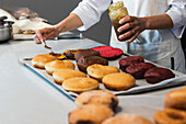 Faceless crop baker spreading sweet jam on vegan sponge cakes while preparing desserts in kitchen of bakery shop