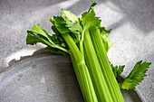 Vibrant green organic celery sticks with leaves, arranged neatly on a textured grey surface, highlighting their freshness and natural appeal.